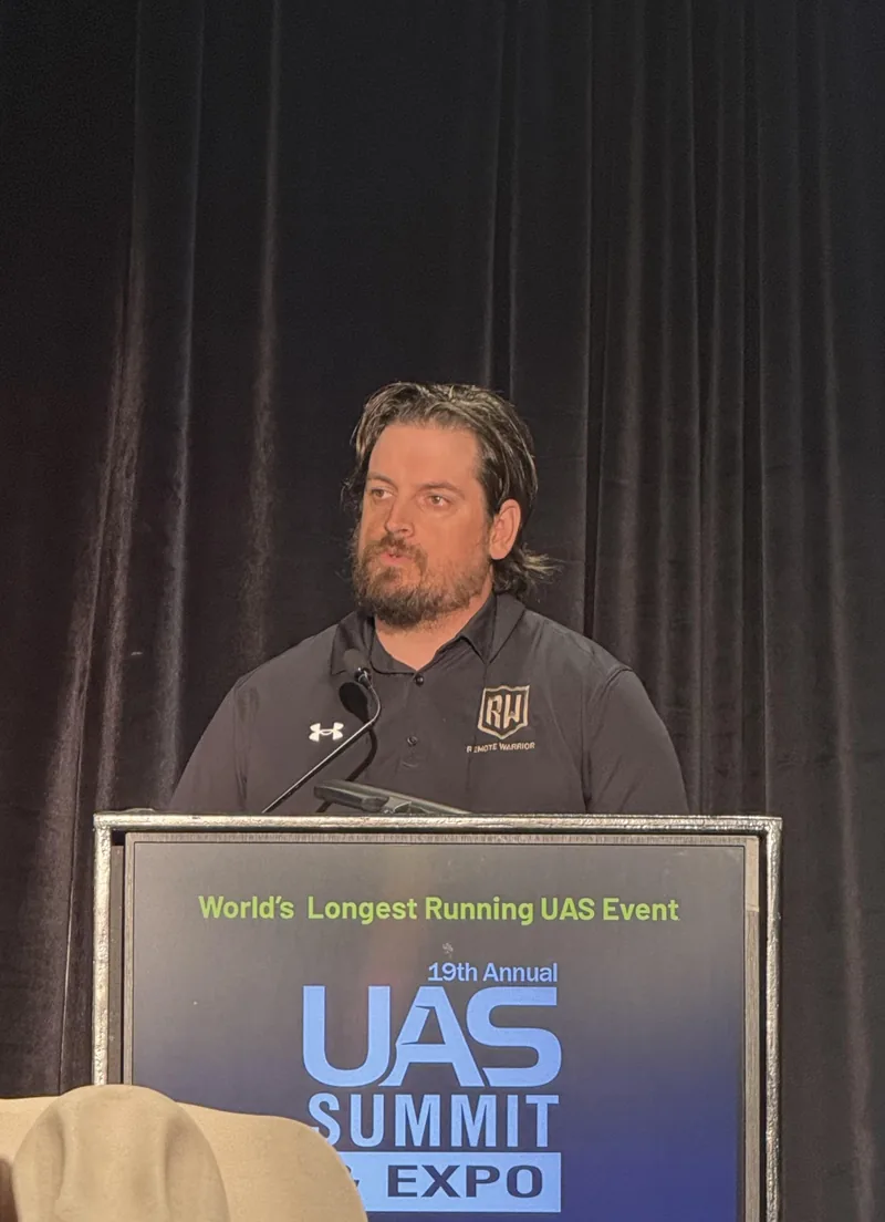 Tanner Yackley speaking at the UAS Summit & Expo, wearing a Remote Warrior polo behind the podium.